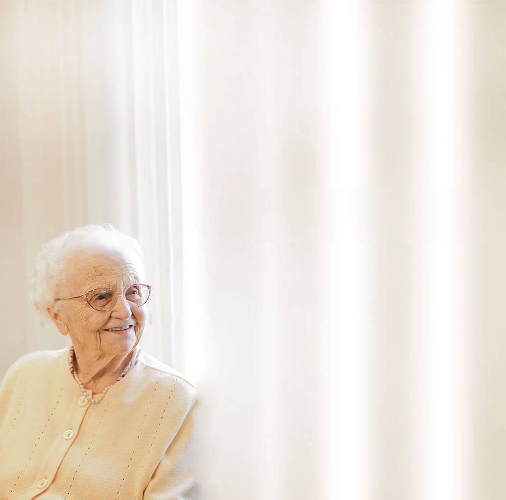 Über uns – Seniorin sitzt for Vorhang